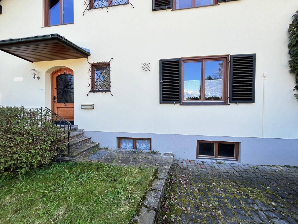 Hauseingang mit Holztür, Fensterläden und kleiner Überdachung.