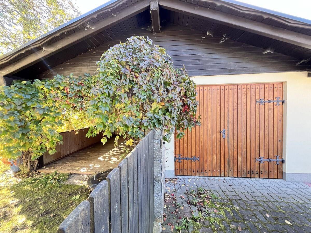 Garage mit rustikalen Holztoren und begrüntem Vordach.
