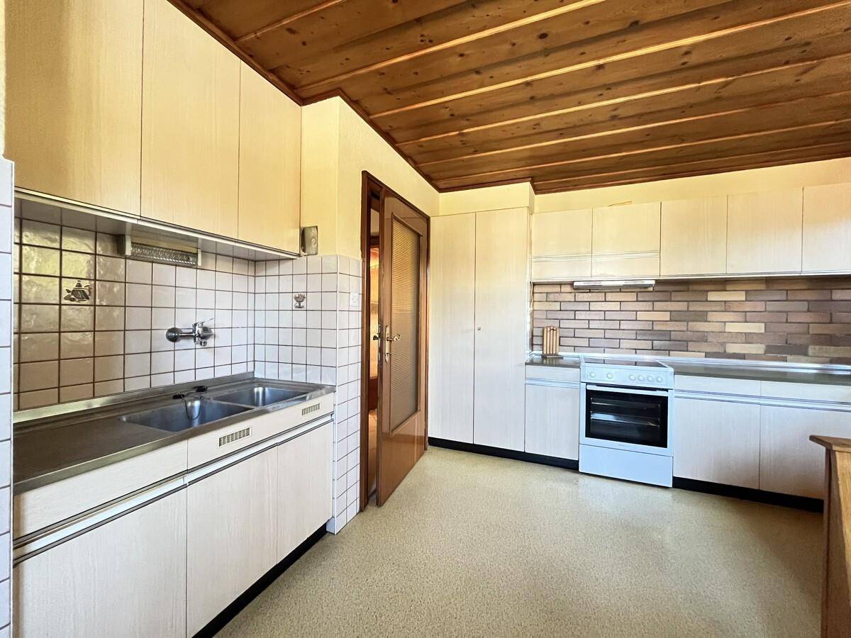 Funktionale Küche mit weißen Schränken, Fliesenrückwand und traditionellem Holzdecken-Design.