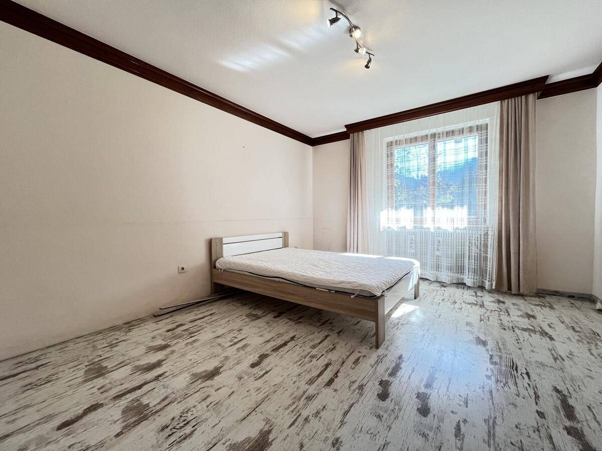 Schlafzimmer mit hellem Holzbett, Laminatboden und großem Fenster für viel Tageslicht.
