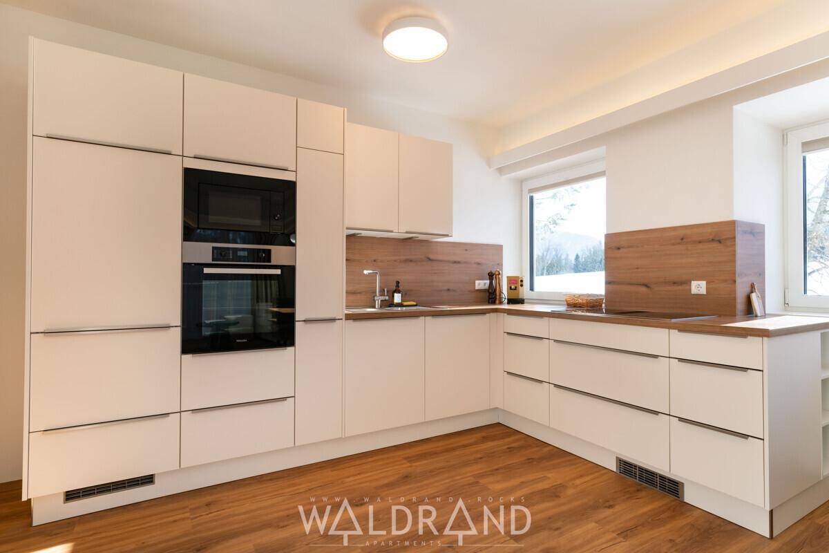 Moderne Einbauküche mit hellen Fronten, integrierten Geräten und Holzboden.