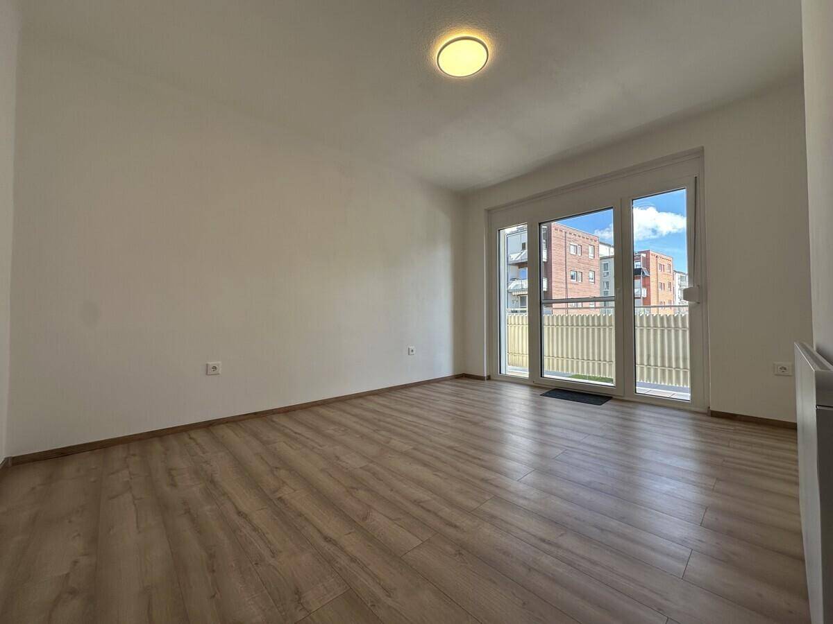 Geräumiges, helles Zimmer mit Laminatboden und Zugang zu einem Balkon, unmöbliert.