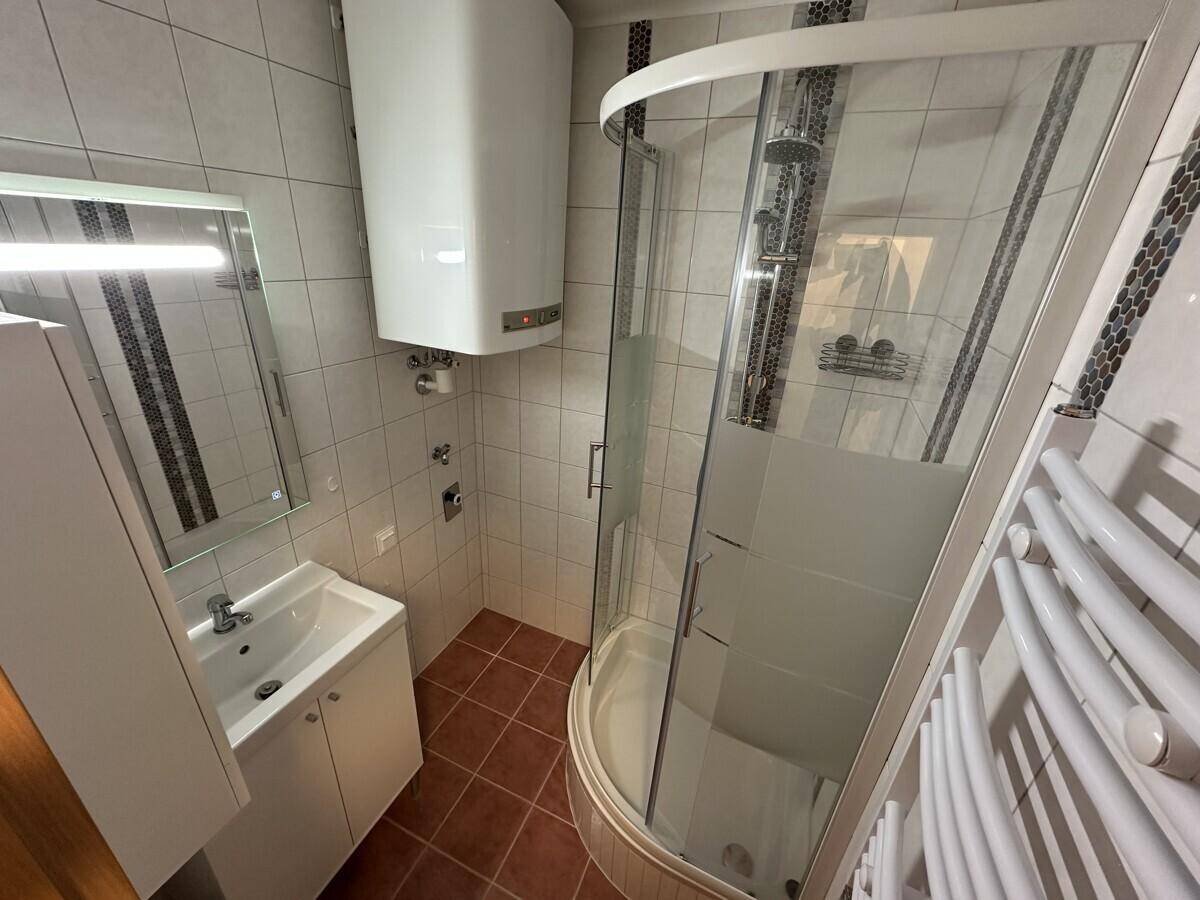 Modernes Badezimmer mit Eckduschkabine, Waschbecken und Wandheizkörper, hell gefliest.