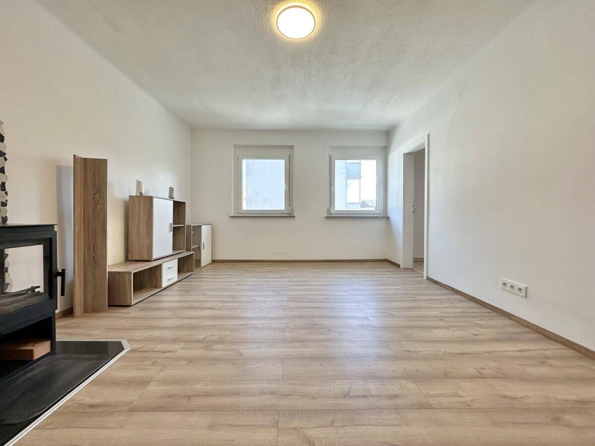 Heller, leerer Wohnbereich mit Laminatboden und zwei Fenstern, bereit zur Einrichtung.