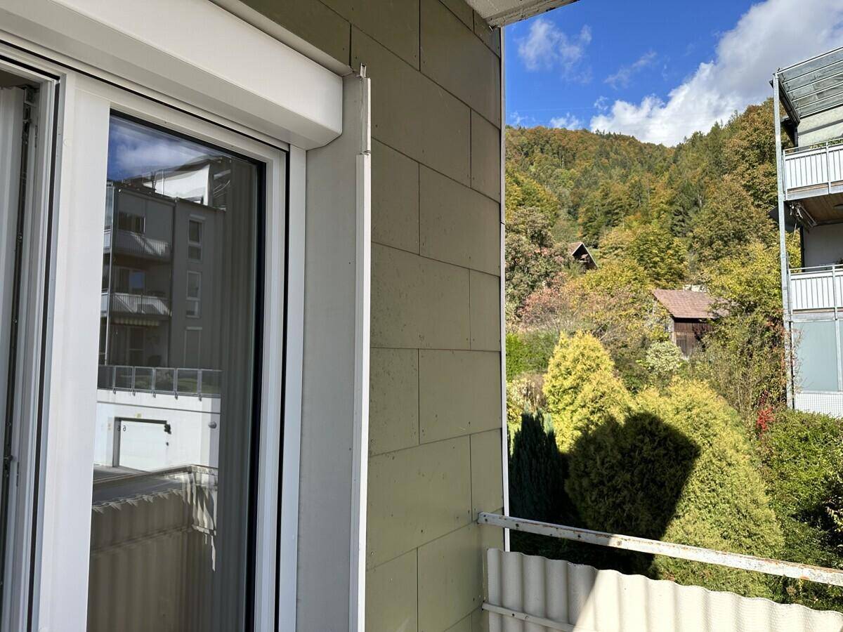 Balkon mit Blick auf bewaldete Hügel und umliegende Gebäude, sonniger Tag.