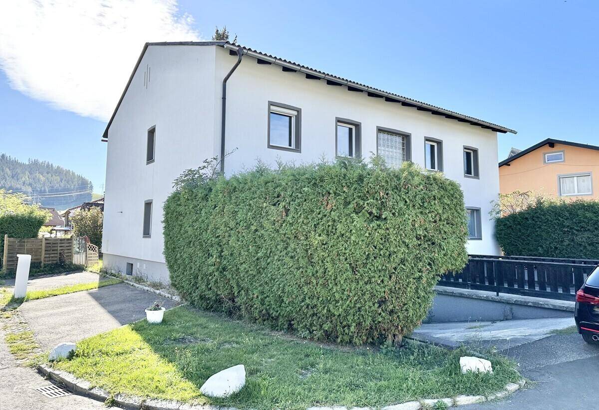 Vorderansicht eines Mehrfamilienhauses mit gepflegter Hecke und Zufahrt.