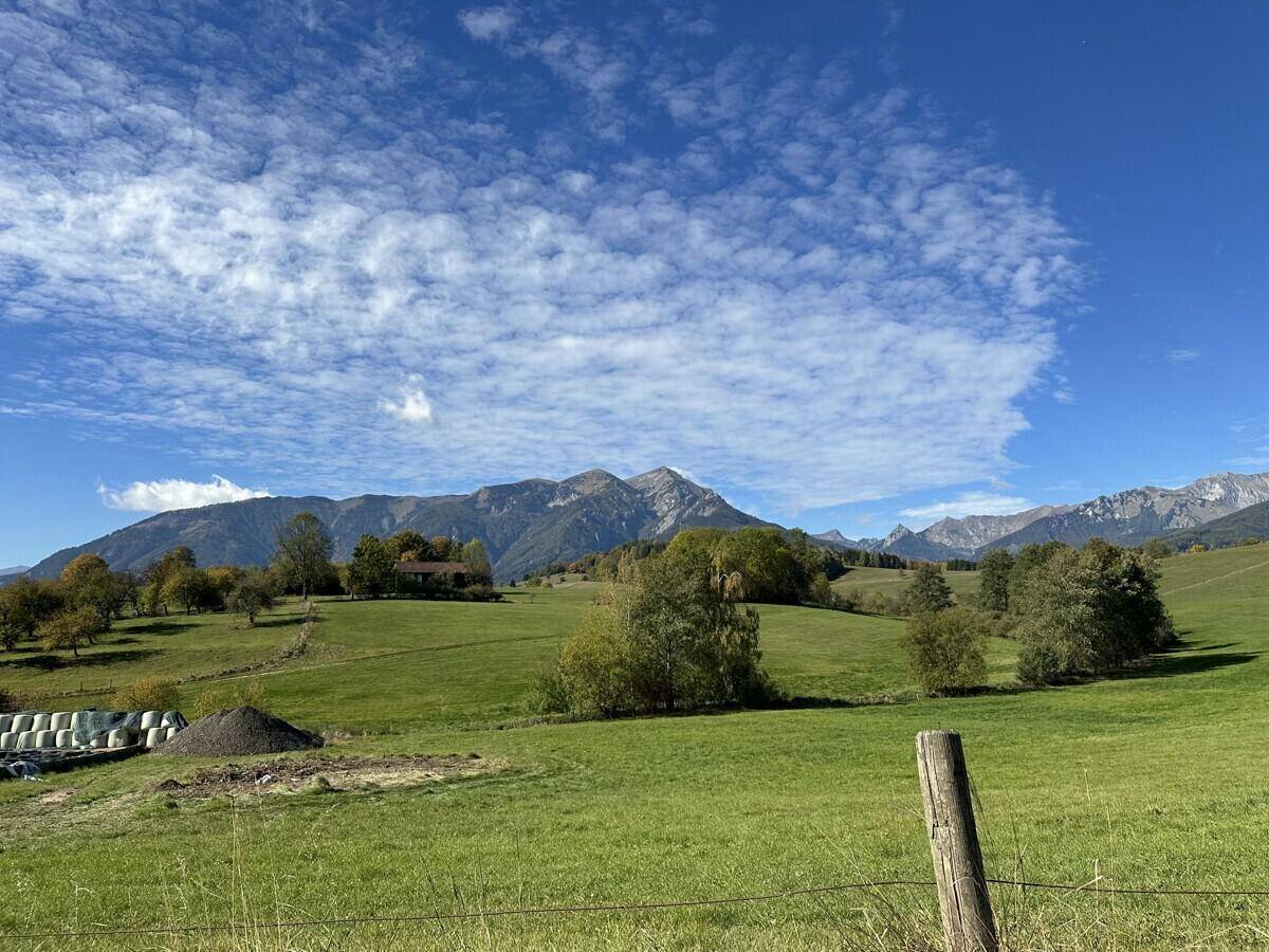 Weitläufige grüne Landschaft mit sanften Hügeln und Bergen unter blauem Himmel.