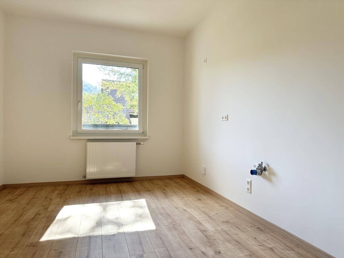 Leerer Raum, vorbereitet für eine Küche, mit Fenster und Holzboden.