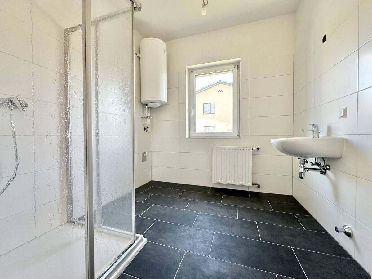 Modernes Badezimmer mit Dusche, Waschbecken, Fenster und dunklen Fliesen.