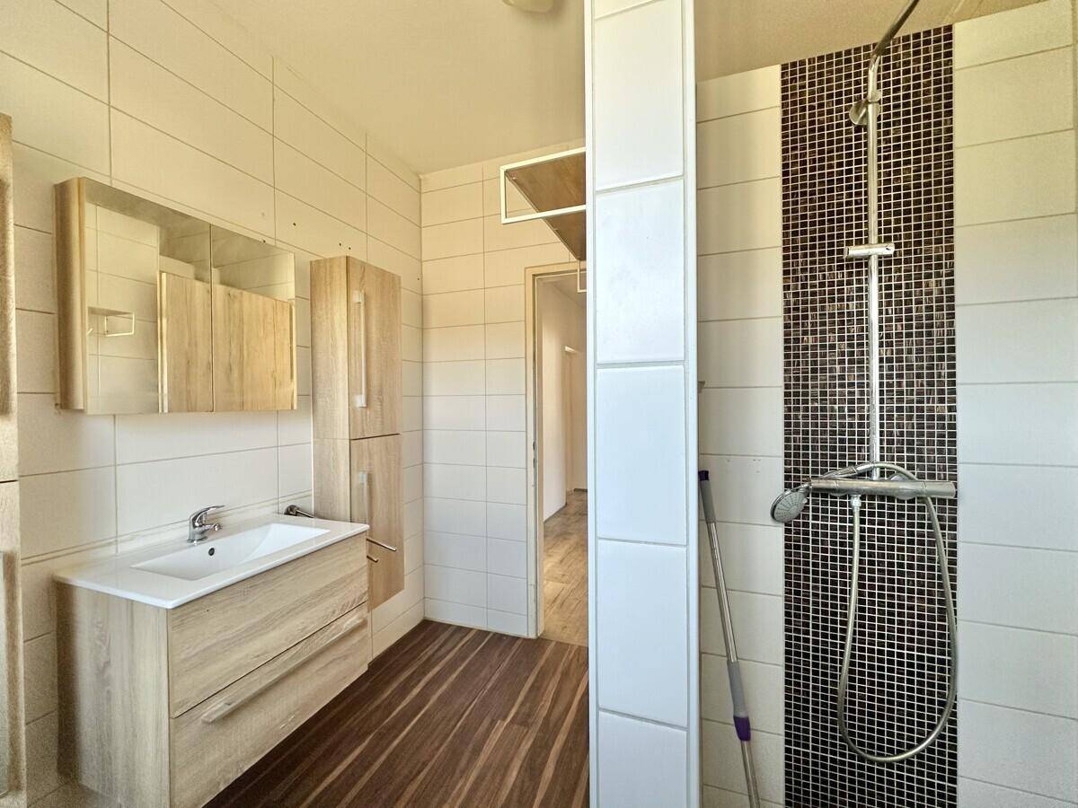 Helles Badezimmer mit Duschkabine, Holzwaschtisch und Spiegelschrank.