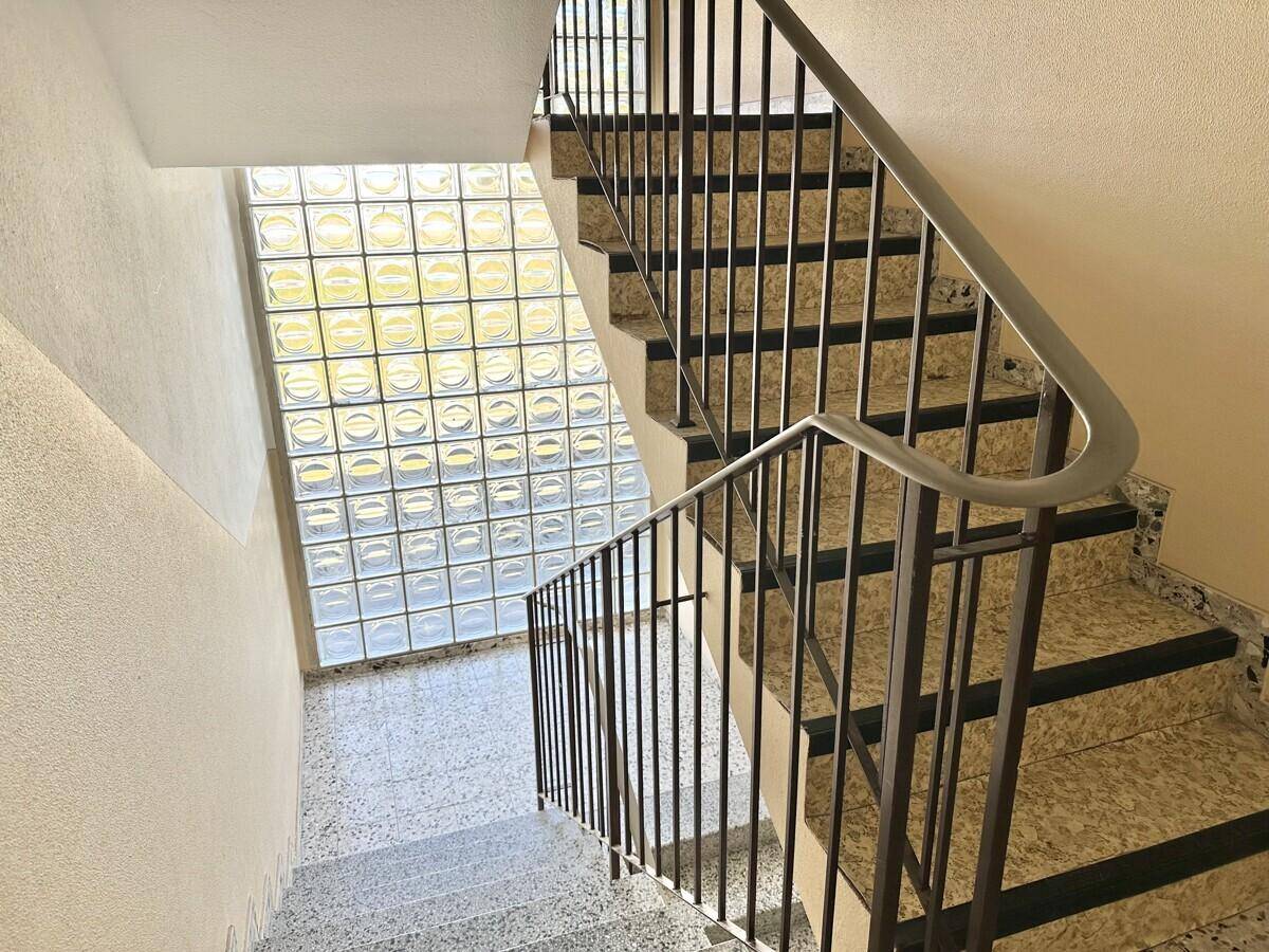 Treppenhaus mit Granitstufen, Metallgeländer und Glasbausteinwand für Tageslicht.