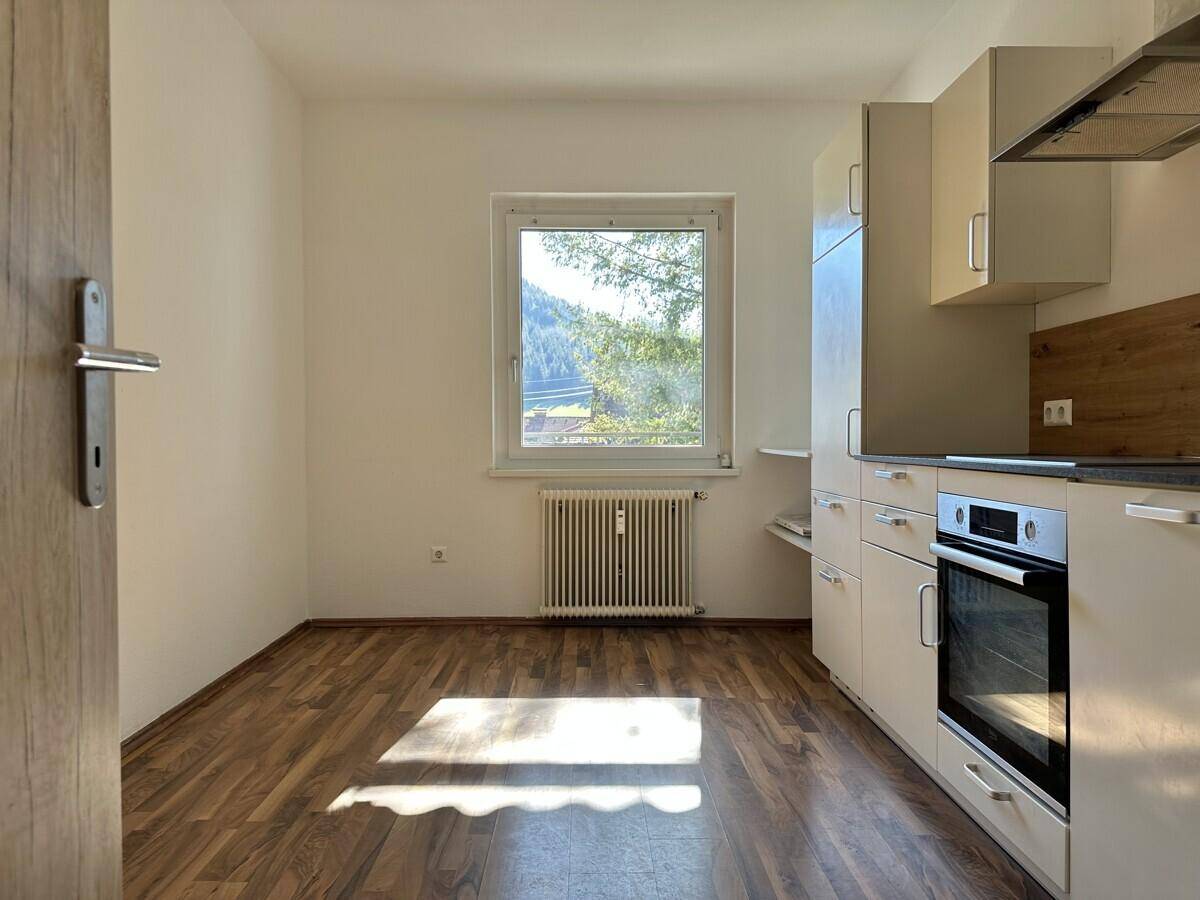 Helle Küche mit Einbauschränken, Ofen und Fenster mit Blick ins Grüne.