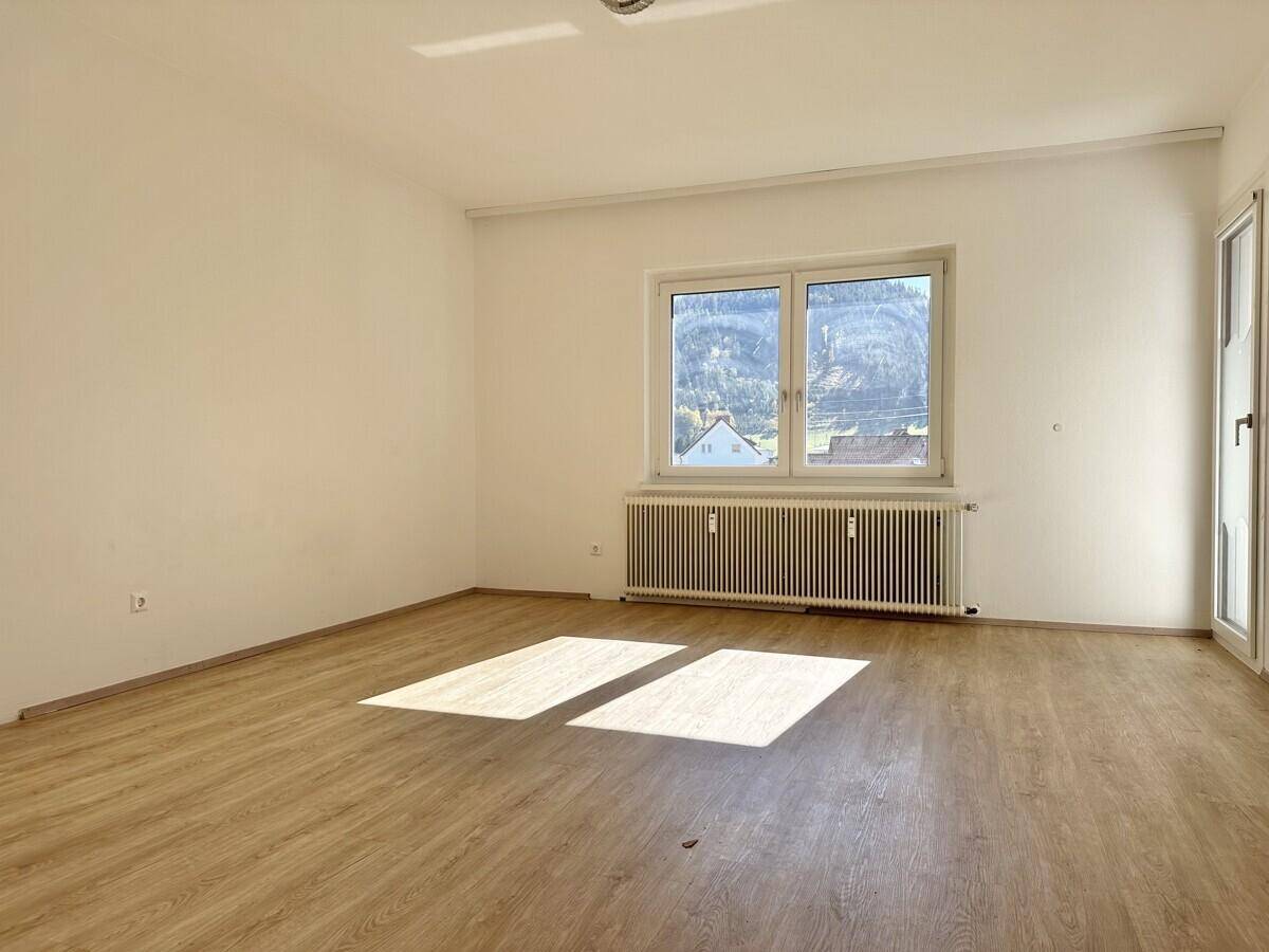 Geräumiges Wohnzimmer mit Laminatboden, großem Fenster und viel Tageslicht.