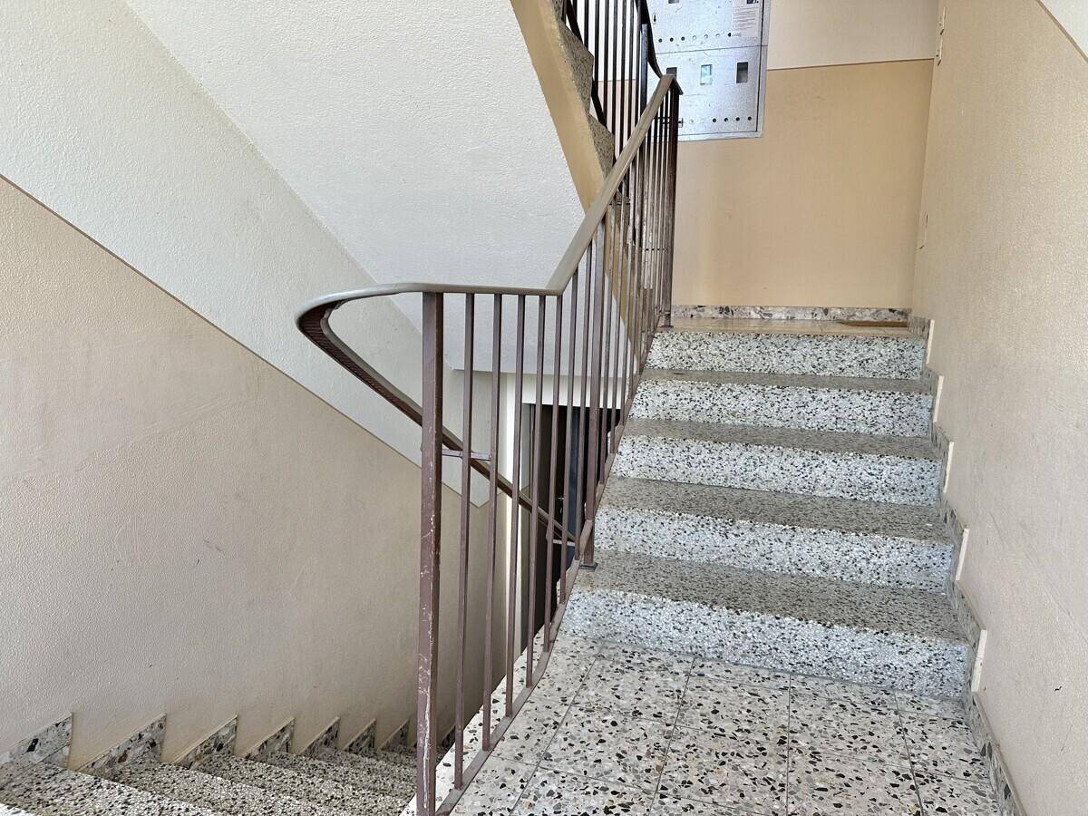 Treppenhaus mit Granitstufen und schlichtem Metallgeländer in einem Mehrfamilienhaus.