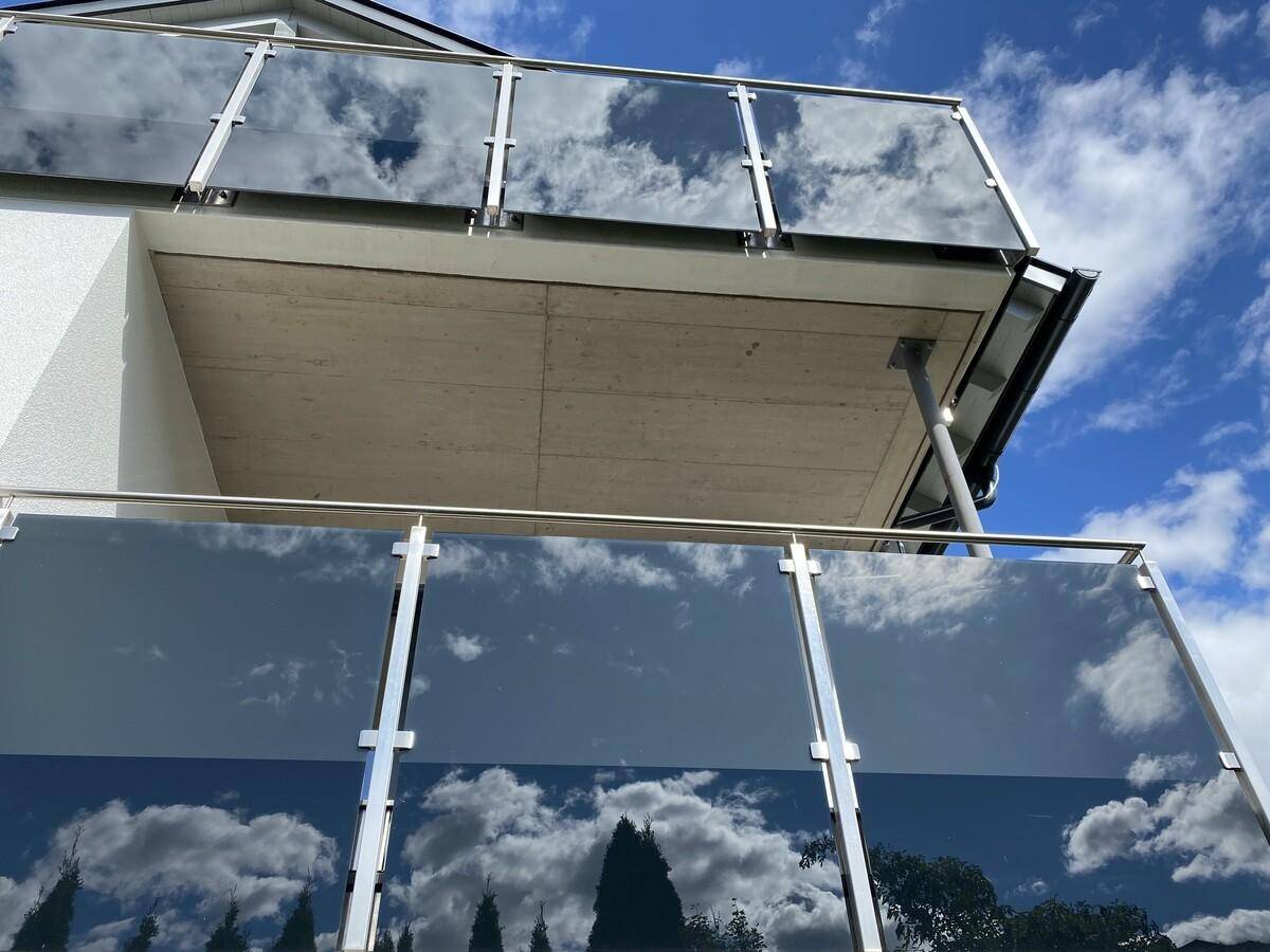Detailansicht eines modernen Balkons mit Glasgeländer und Spiegelung des Himmels.
