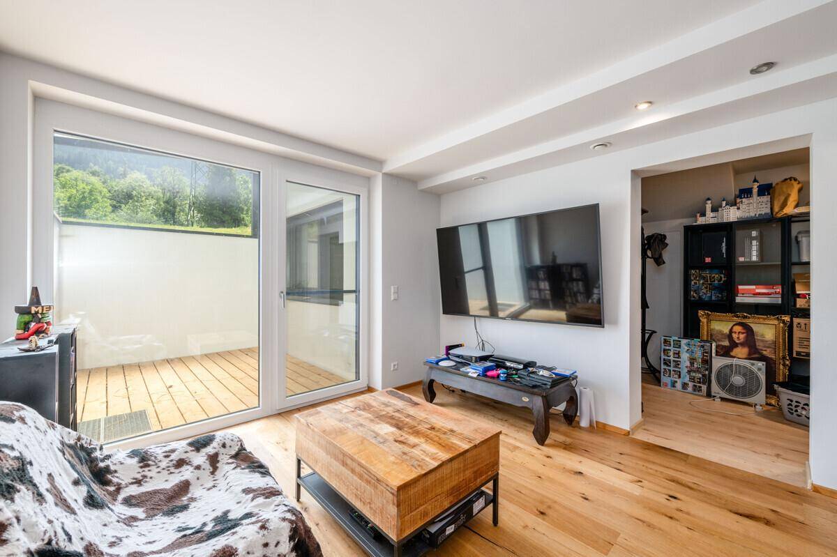 Helles Wohnzimmer mit Holzboden, großem Fernseher und Zugang zu einer Terrasse.