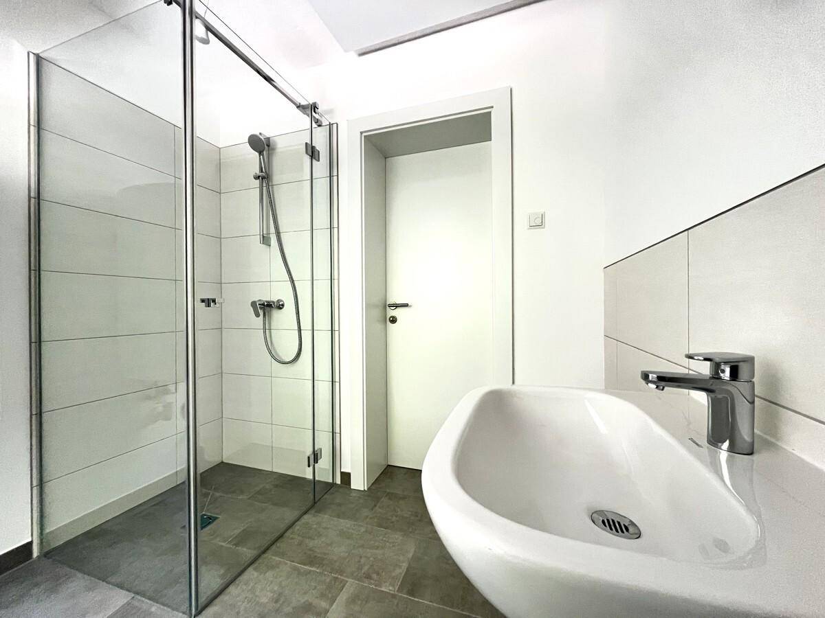 Modernes Badezimmer mit ebenerdiger Dusche, Einzelwaschbecken und hellen Fliesen.