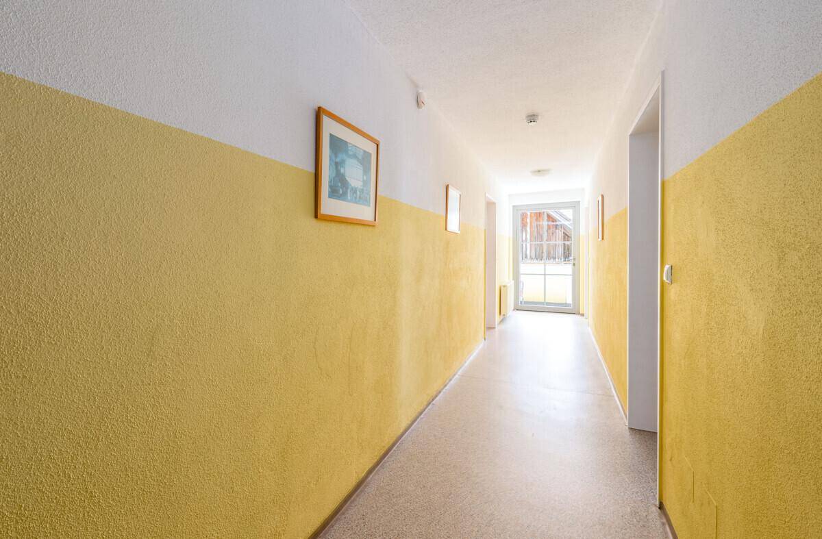 Heller Flur mit gelb-weißen Wänden und einem Fenster am Ende, das Tageslicht spendet.