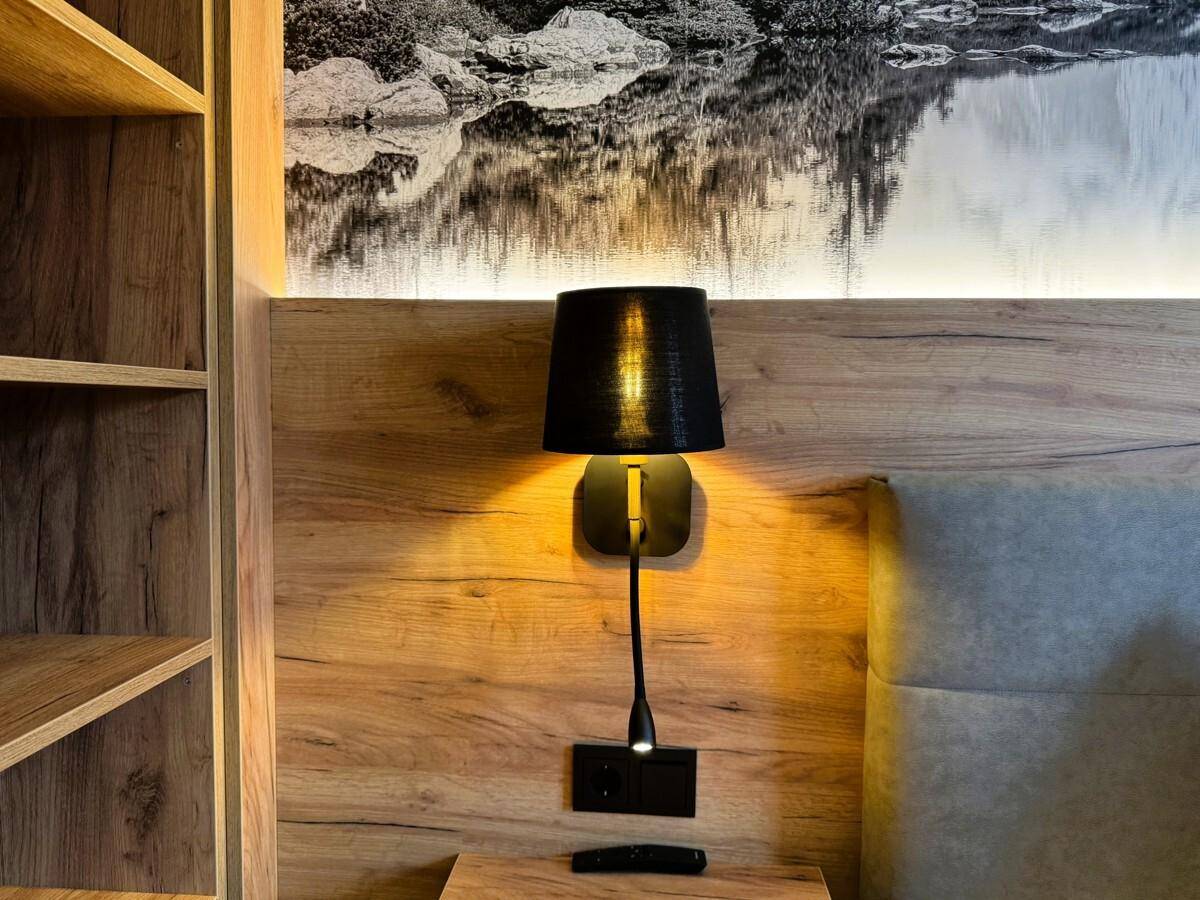 Detailansicht des Nachttisches mit Leselampe und Holzwandverkleidung im Schlafzimmer.