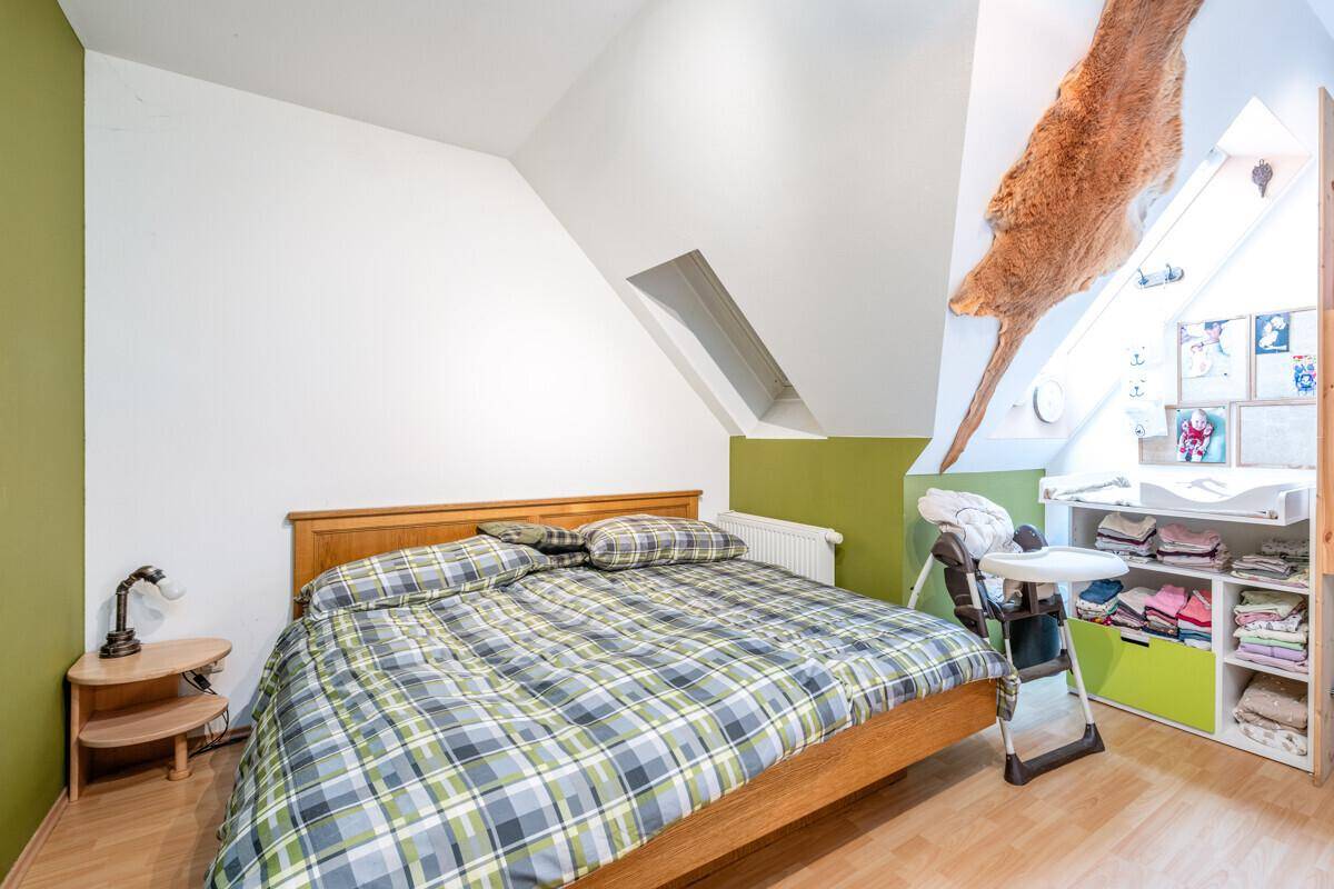 Schlafzimmer mit Holzbett, karierter Bettwäsche und Wickelbereich unter der Dachschräge.
