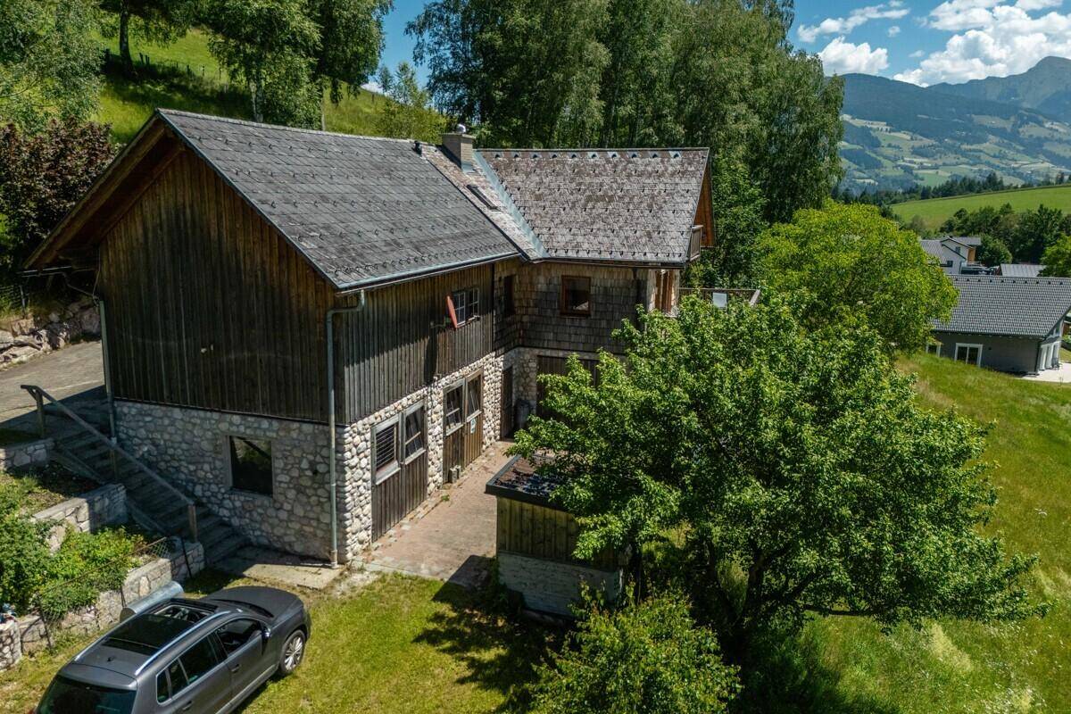 Ansicht des Chalets von der Seite mit Steinfundament, Holzelementen und einem geparkten Auto auf der Auffahrt.