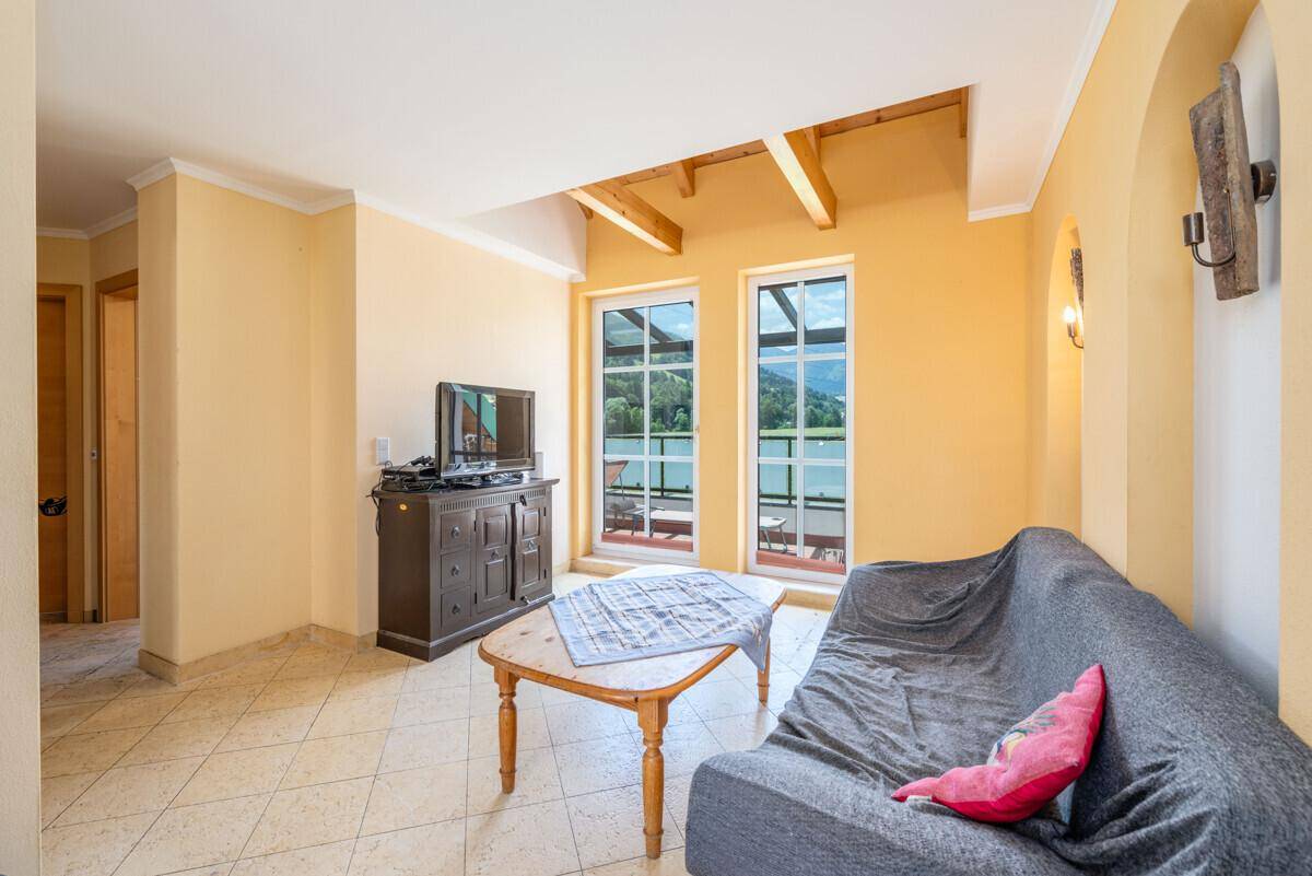 Gemütlicher Wohnbereich mit Sofa, Fernseher und Zugang zu einem Balkon mit Bergblick.