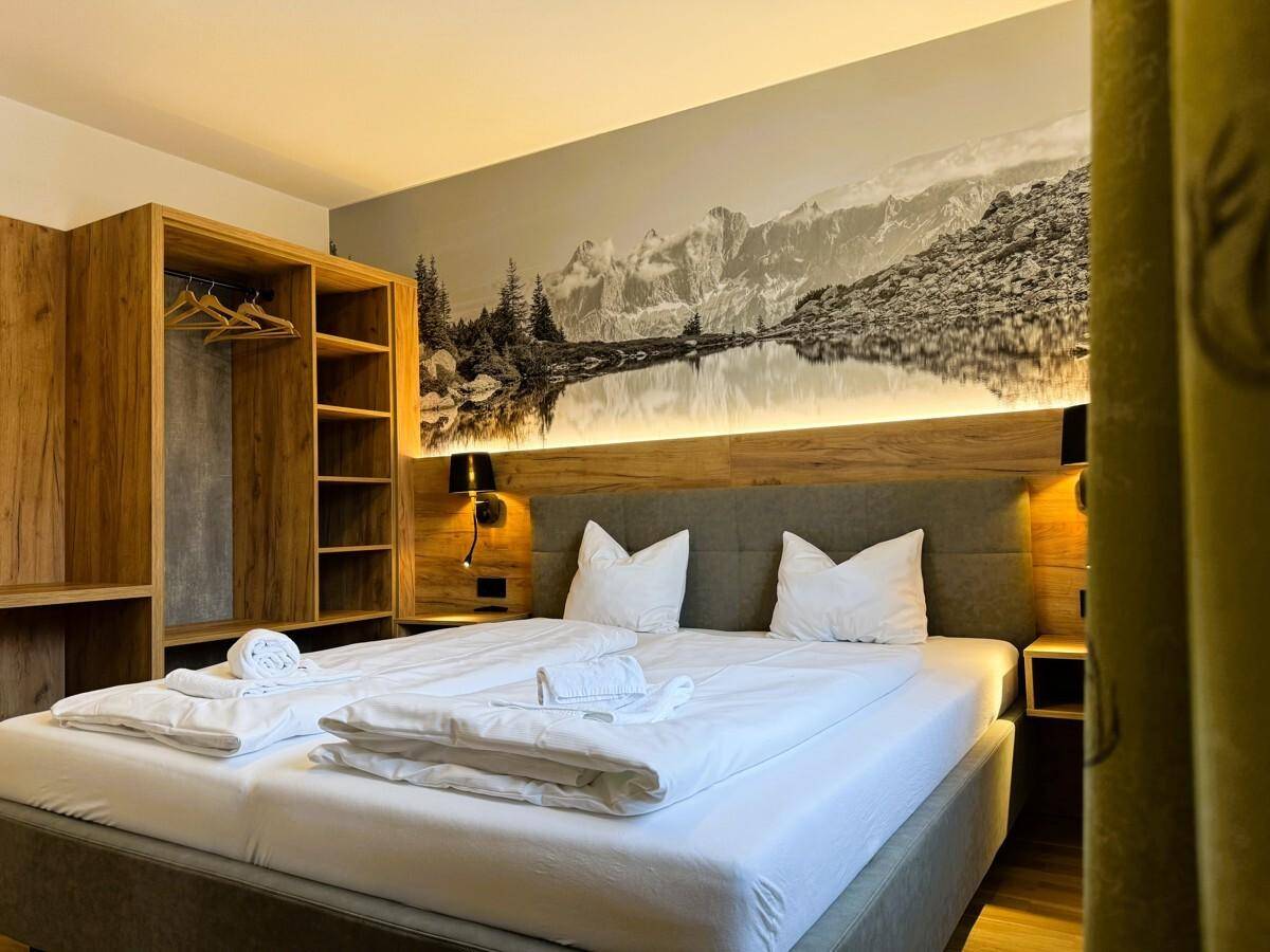 Gemütliches Schlafzimmer mit Doppelbett, Holzelementen und Wandbild einer Berglandschaft.