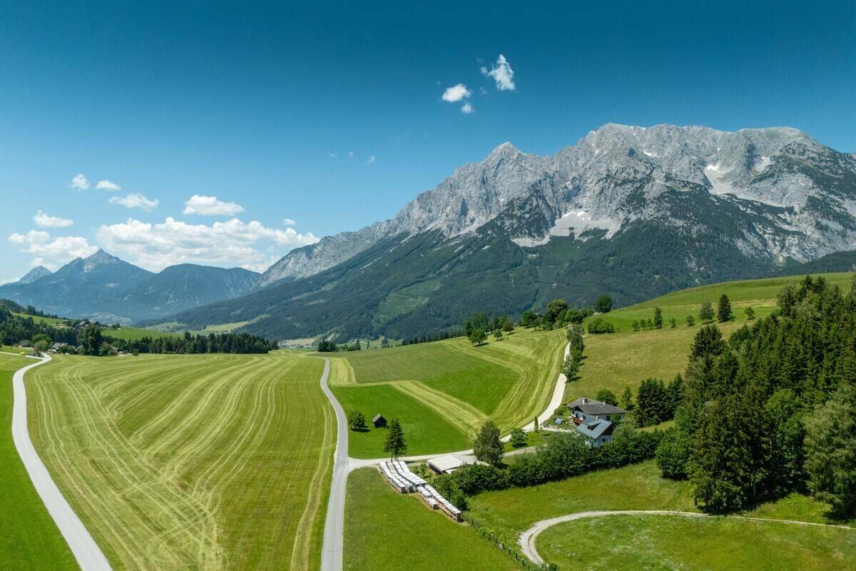 Luftaufnahme eines Hauses in einer weiten grünen Landschaft mit majestätischen Bergen im Hintergrund.