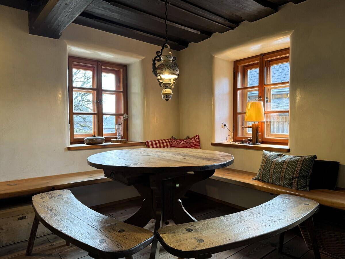 Rustikaler Essbereich mit rundem Holztisch und eingebauten Holzbänken, umgeben von warmem Licht.