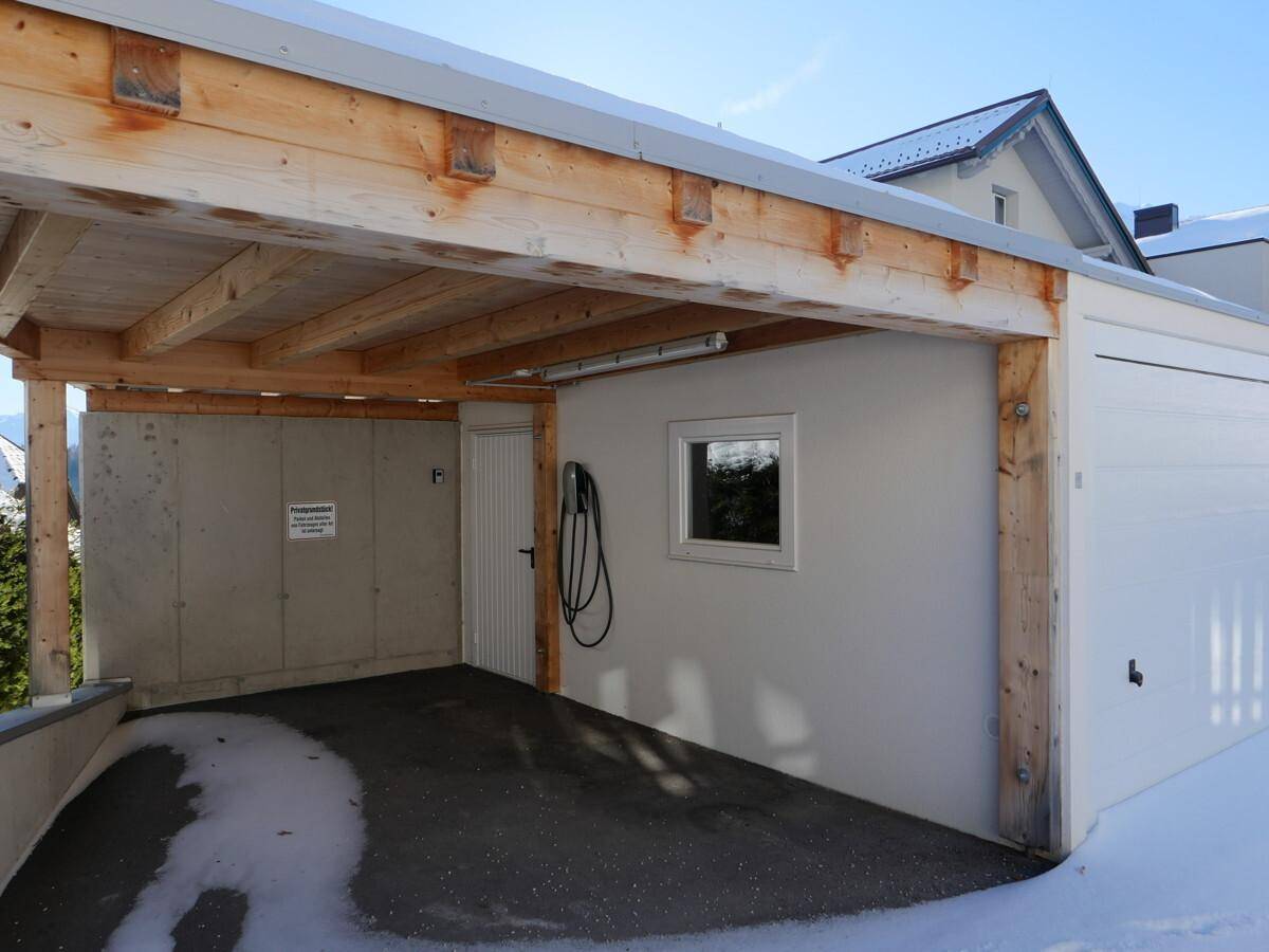 Innenansicht des Carports mit Holzbalken, kleinem Fenster und einer Ladestation für Elektrofahrzeuge.