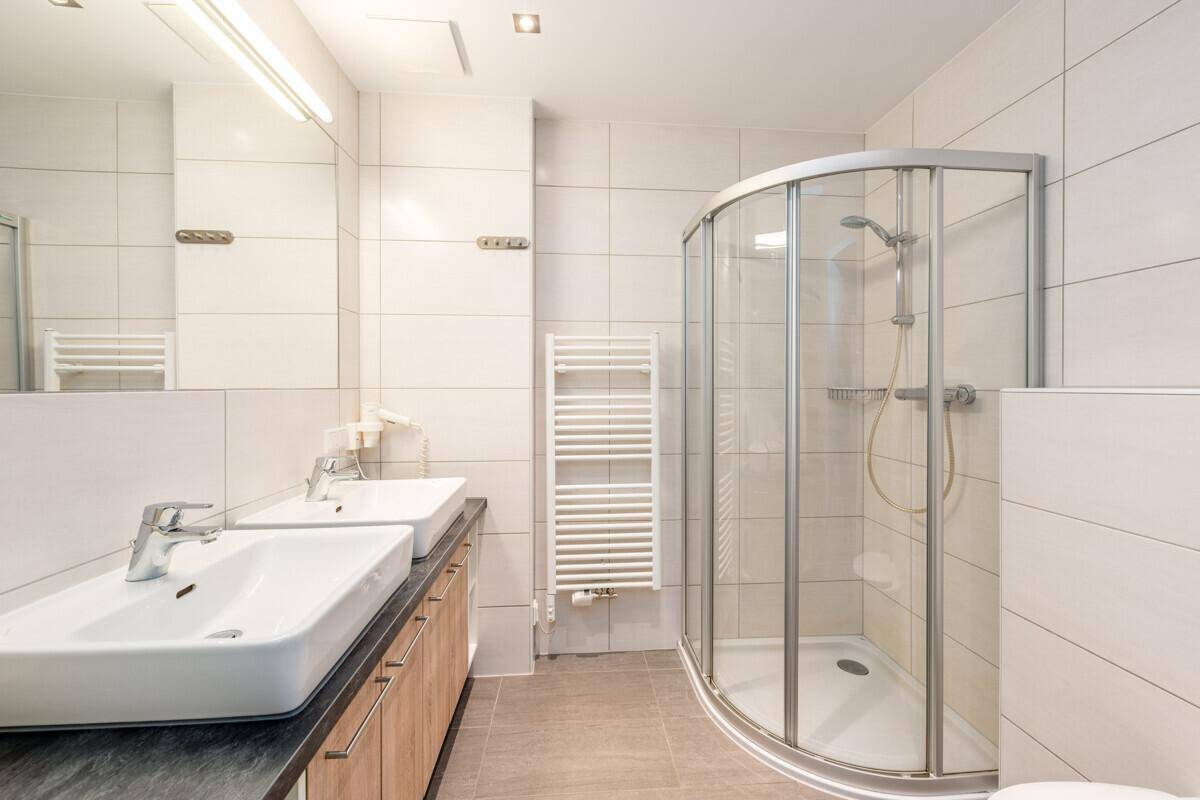 Modernes Badezimmer mit Doppelwaschbecken, Duschkabine und beheiztem Handtuchhalter.