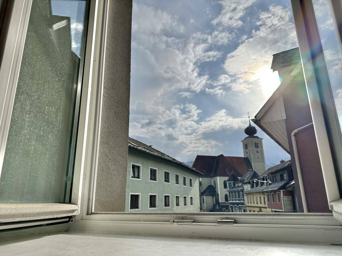 Blick aus dem Fenster auf eine malerische Stadt mit Kirchturm und bewölktem Himmel.