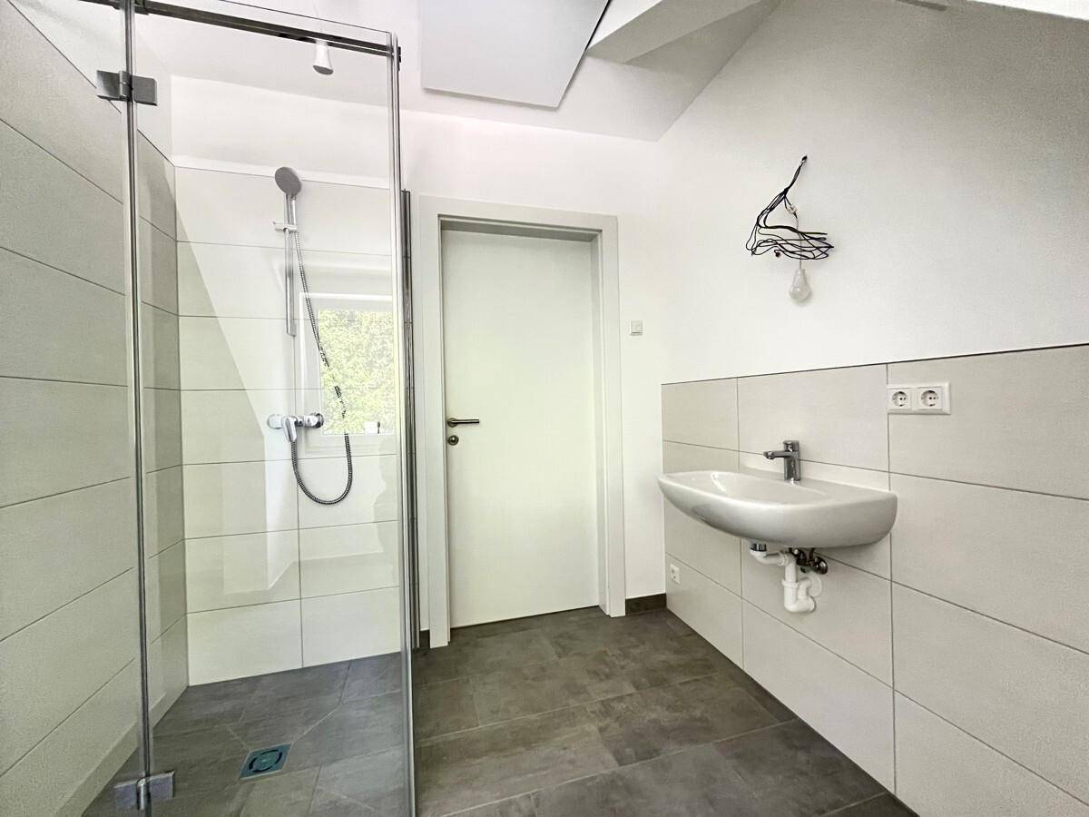 Modernes Badezimmer mit ebenerdiger Dusche, Einzelwaschbecken und hellen Fliesen.