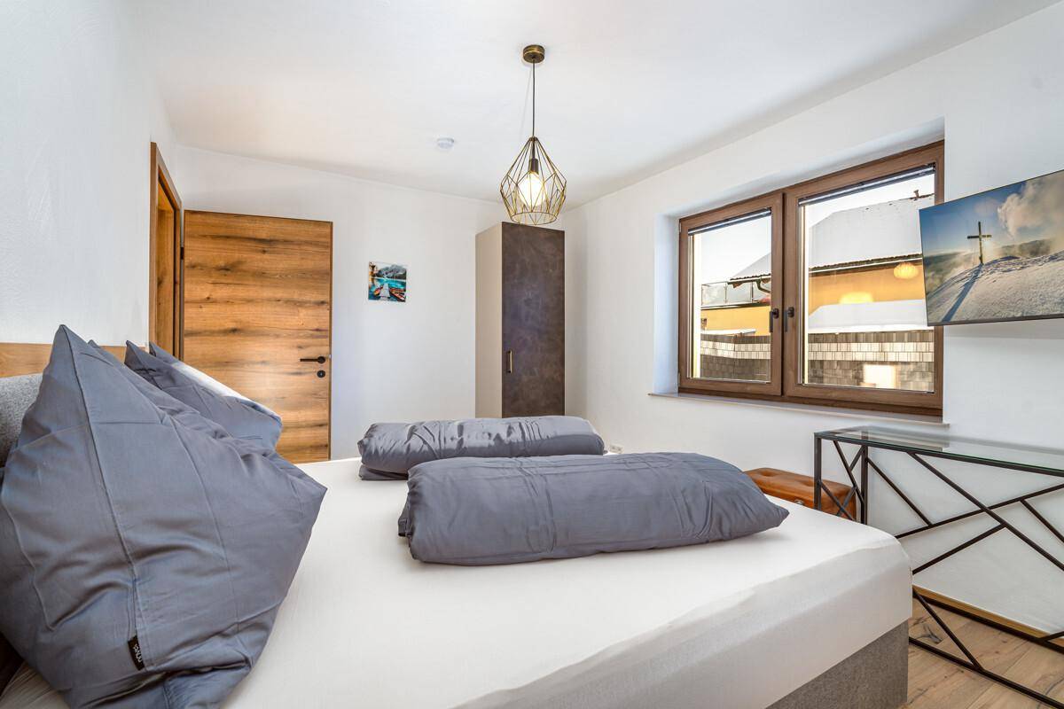 Helles Schlafzimmer mit Doppelbett, Holzboden und Fenster mit Blick nach draußen.