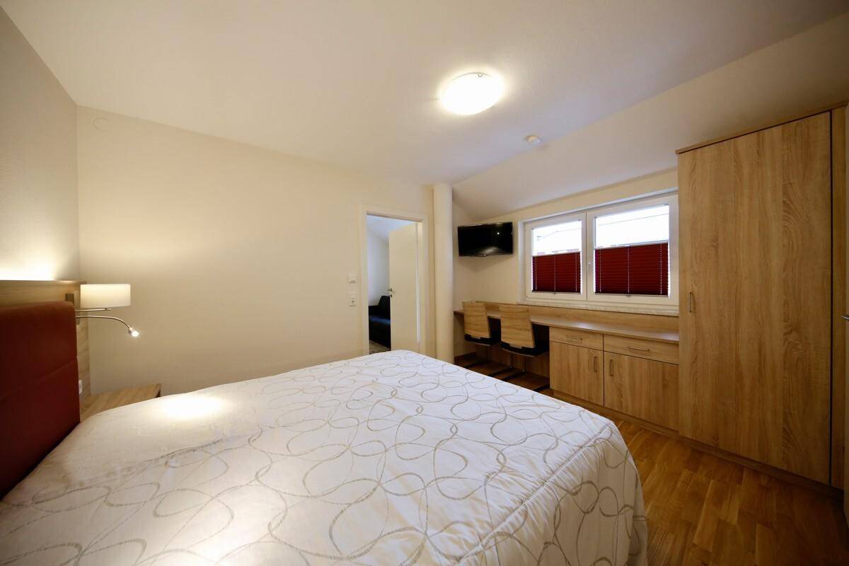 Gemütliches Schlafzimmer mit Doppelbett, Holzmöbeln und einem Fenster, das natürliches Licht hereinlässt.