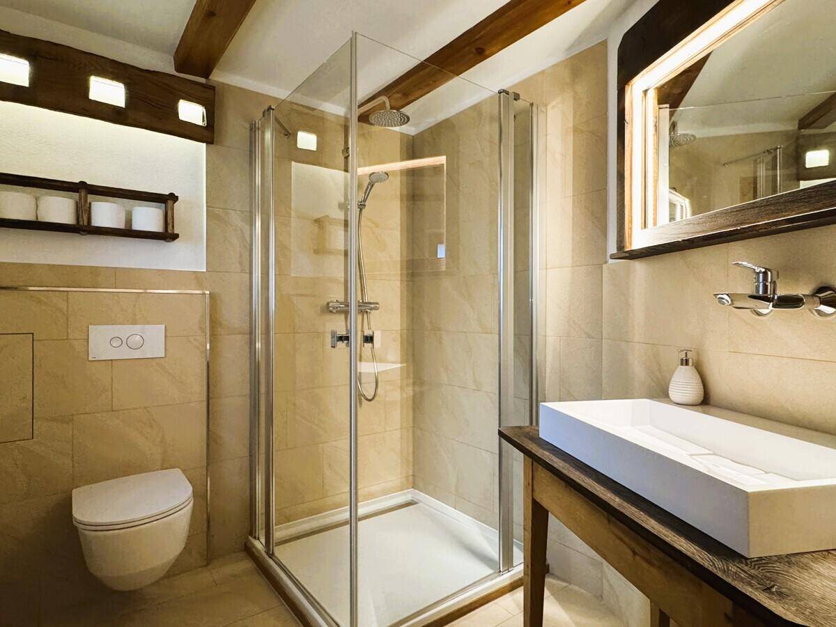 Modernes Badezimmer mit begehbarer Dusche, Wand-WC und stilvollem Waschbecken auf Holzunterschrank.