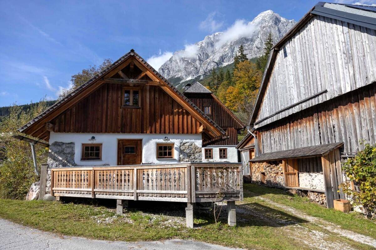 Traditionelles Holzhaus mit Balkon und Steinsockel vor einer beeindruckenden Bergkulisse.