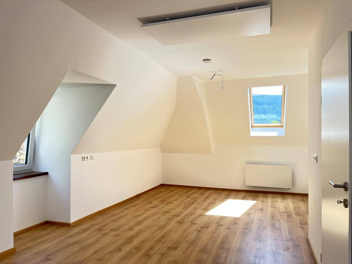 Geräumiges Zimmer im Dachgeschoss mit Laminatboden, Schrägdach und einem Dachfenster mit Weitblick.