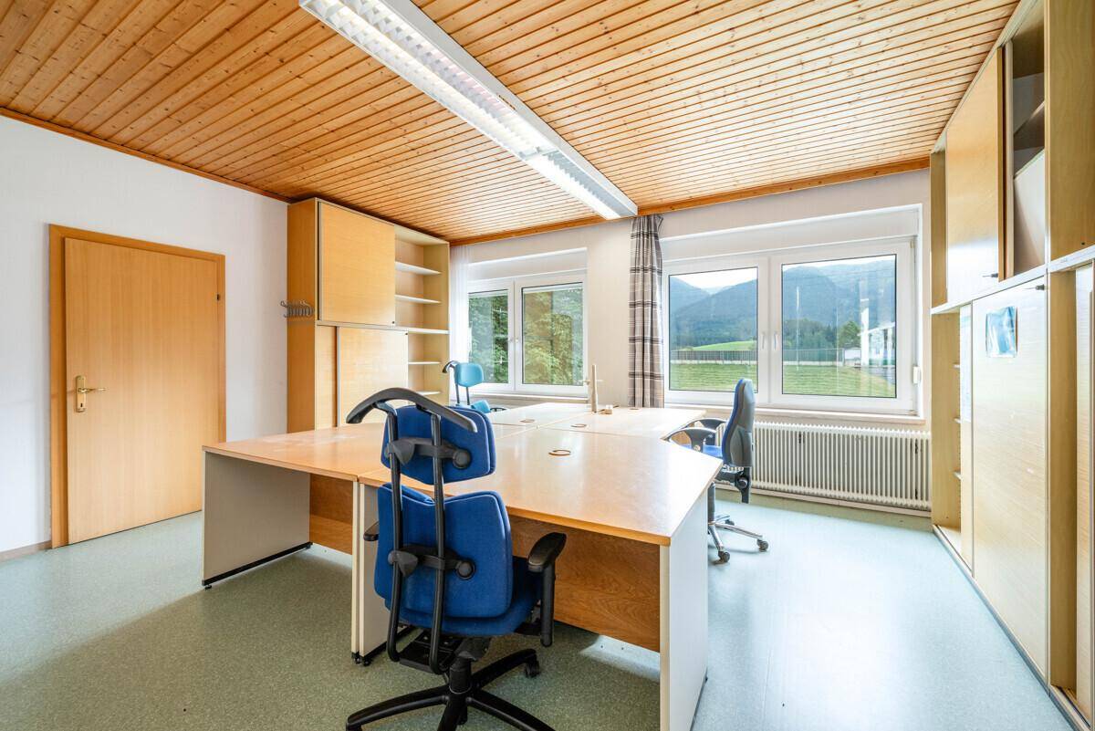 Büro mit Holzdecke, Schreibtischen und Blick auf die grüne Landschaft und Berge.