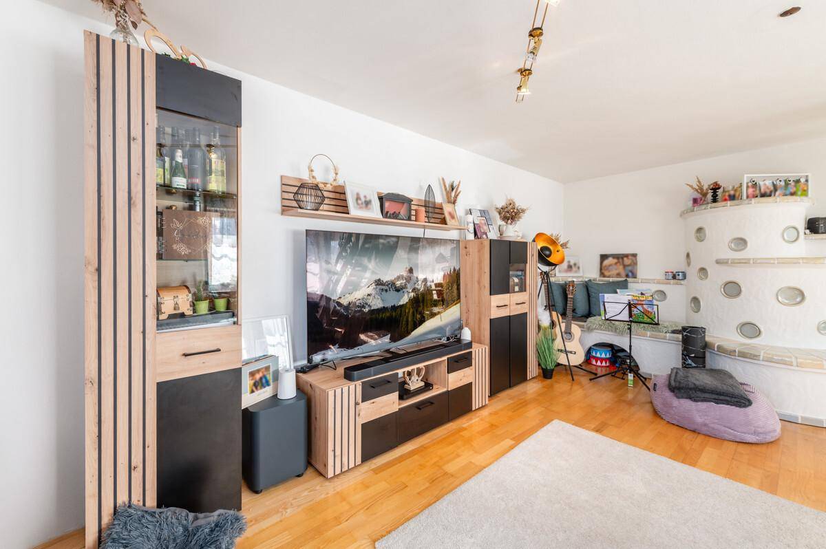 Wohnzimmer mit TV-Möbel, traditionellem Kachelofen und hellem Holzboden.