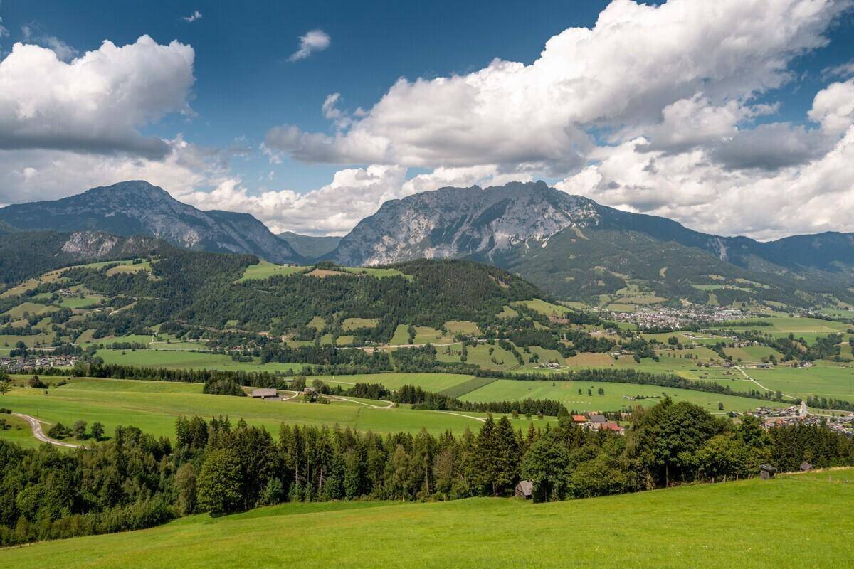Malerische Berglandschaft mit grünen Tälern, Wäldern und kleinen Siedlungen unter blauem Himmel.