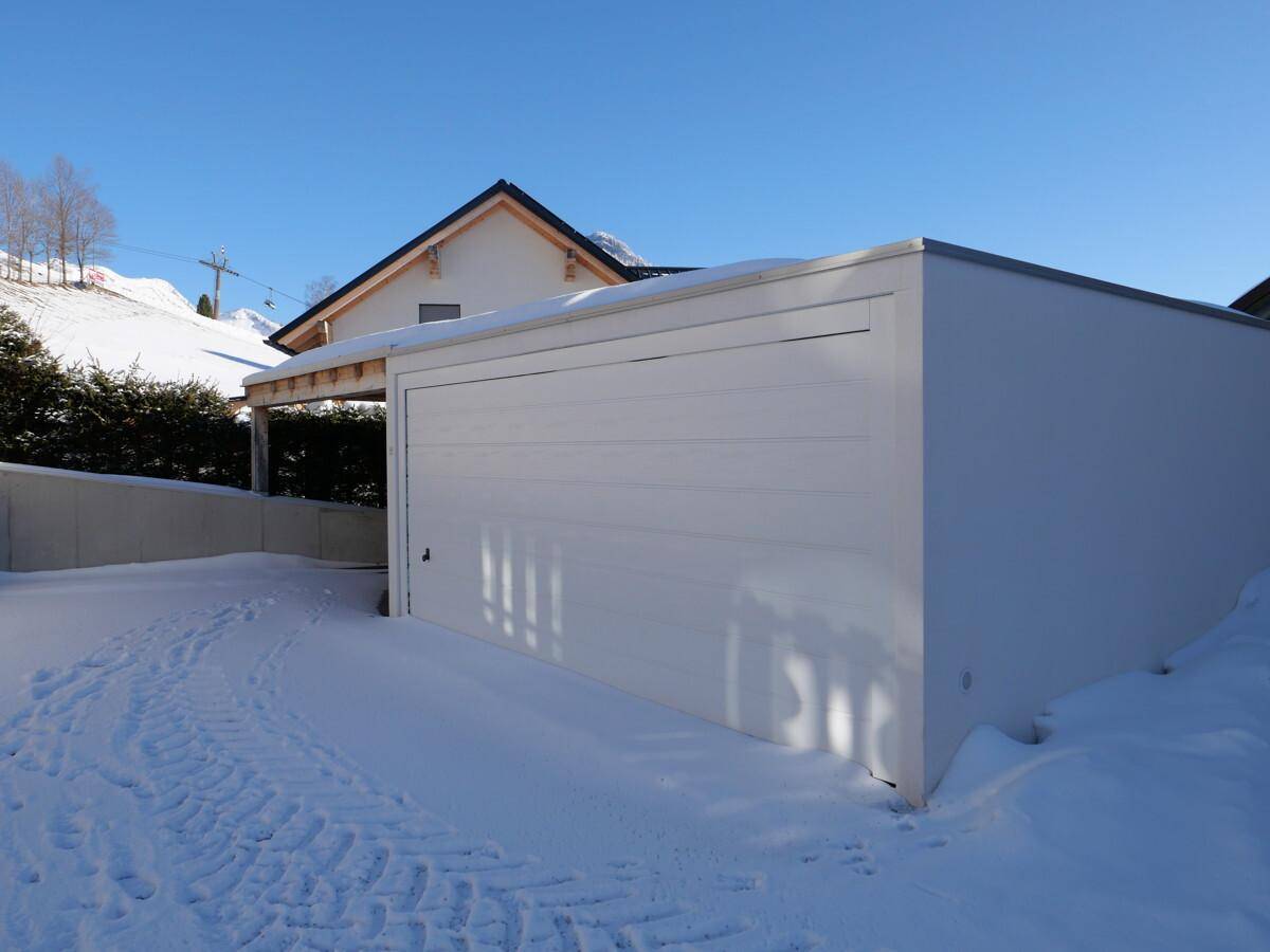 Außenansicht der modernen Garage und des Carports im Winter mit Schnee und sonnigem Wetter.