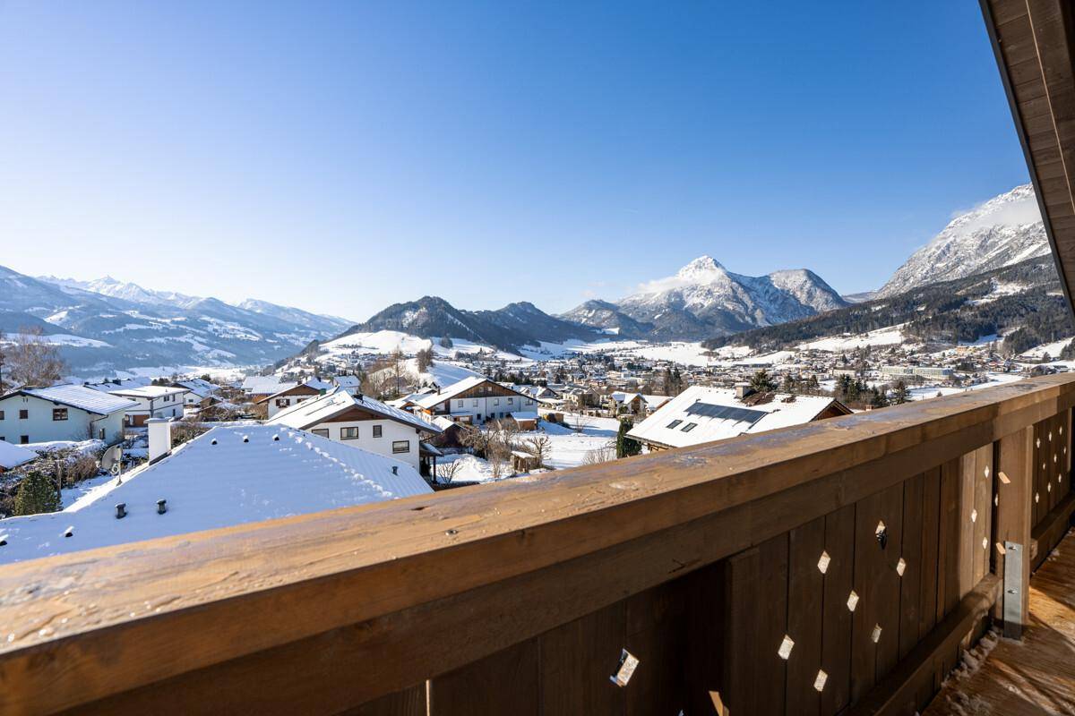 Breiter Holzbalkon mit Panoramablick auf die verschneite Berglandschaft und das Dorf.