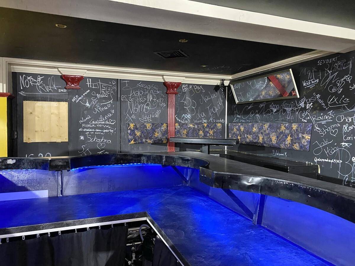 Bartheke mit blauer Beleuchtung und dunklen Wänden, die mit Graffiti und gemusterten Tapeten bedeckt sind.