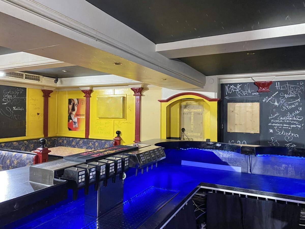 Gesamtansicht des Barbereichs mit beleuchteter Theke und Sitzgelegenheiten an gelben Wänden mit Graffiti.