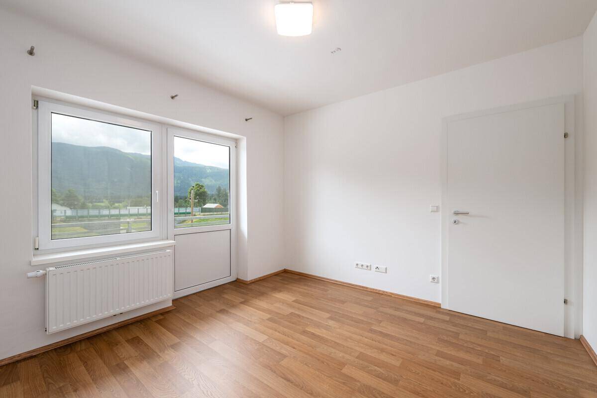 Helles Zimmer mit Laminatboden, weiß gestrichenen Wänden und Fenster mit Bergblick.