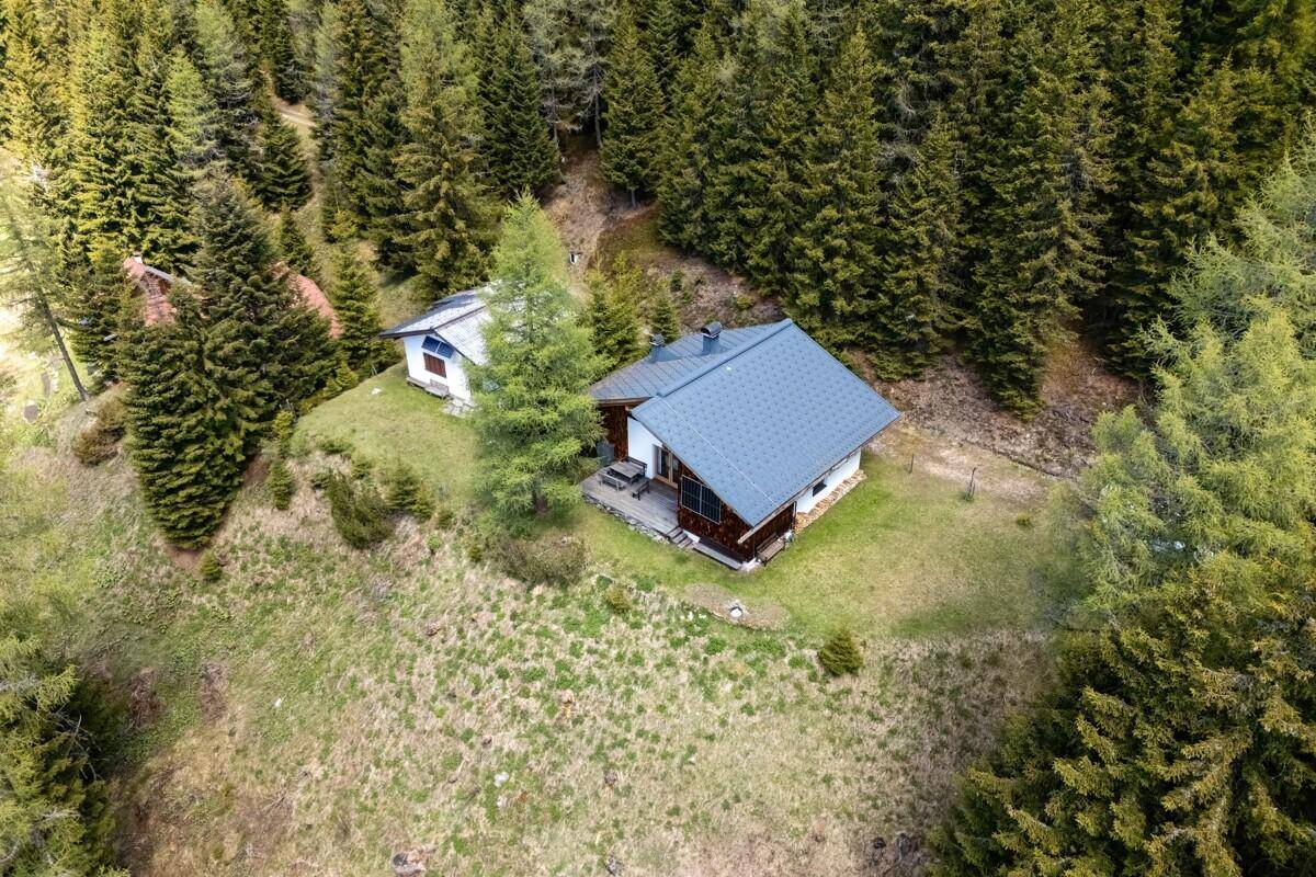 Luftaufnahme einer idyllischen Hütte im Wald, eingebettet in eine grüne Berglandschaft.