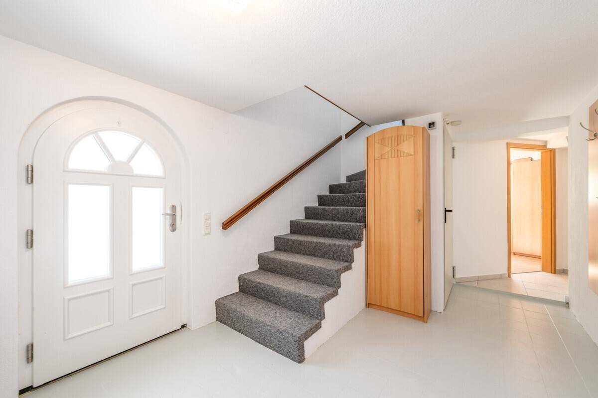 Heller Eingangsbereich mit Treppe und weißer Eingangstür, führt zu weiteren Räumen.