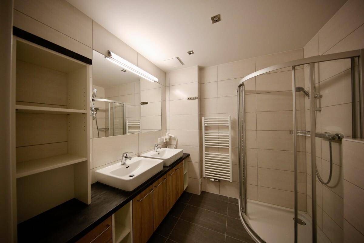 Modernes Badezimmer mit Doppelwaschbecken, Duschkabine, beheiztem Handtuchhalter und großen Fliesen.