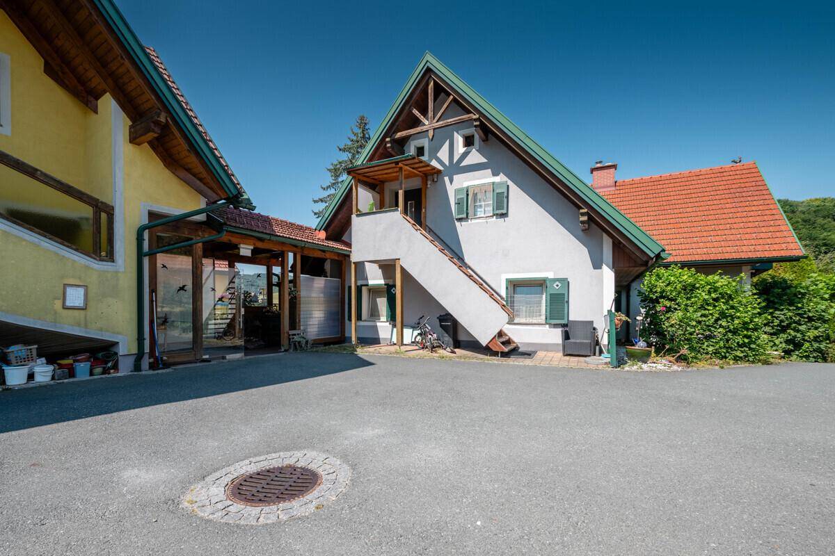 Fassade eines Gebäudes mit Außentreppe und traditionellen grünen Fensterläden, umgeben von viel Grün.
